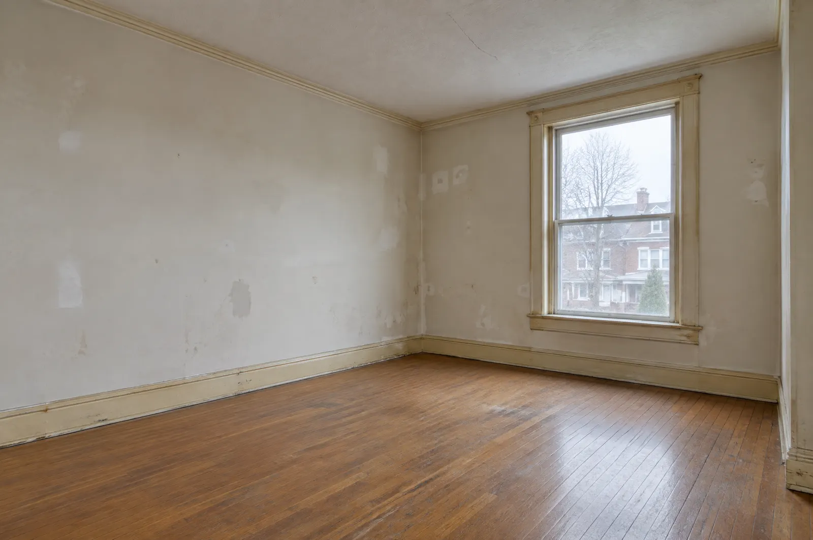 Living room of a Toronto semi-detached house before renovation: patched walls, yellowed trim, worn floor